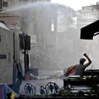 A man holding a rainbow flag throws stones as riot police use water cannon to disperse people taking part in the Gay Pride parade on Sunday in the Istiklal street near the Taksim square in Istanbul. Riot police in Istanbul used tear gas and water cannon to disperse thousands of participants in the Gay Pride parade. | AFP-JIJI