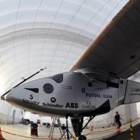 A ground crew member (right) walks near the Solar Impulse 2 in a mobile hanger at Nagoya airport Wednesday. The record-breaking plane landed safely in Nagoya on Monday1 on an unscheduled stop caused by bad weather over the Pacific. It now needs wing repair before setting off for Hawaii in mid-June. | AFP-JIJI