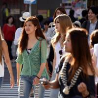 Three 19-year old pedestrians (left) cross a crowded intersection in Tokyo\'s Shibuya Ward on Thursday, the same day the Lower House passed a bill to lower the voting age to 18. | SATOKO KAWASAKI