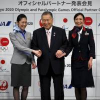 Former Prime Minister Yoshiro Mori, leader of the Olympic organizing committee, greets flight attendants from All Nippon Airways Co. (left) and Japan Airlines Co. at the Tokyo 2020 Olympic and Paralympic Games Official Partner ceremony in Tokyo on Monday. ANA and JAL are the first two entities listed as Tokyo 2020 Official Partners, the second domestic tier in the lucrative Tokyo 2020 Sponsorship Program. | REUTERS
