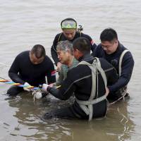 Divers help a passenger to safety after a cruise ship sank in heavy wind and rain on the Yangtze River in Jianli, China, late Monday. With around 450 people missing Tuesday and part of the hull still above water, rescuers believed others could still be alive inside after knocking was heard, reports said. | REUTERS