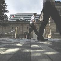 Pedestrians pass the Bank of Japan headquarters in Tokyo in May. The BOJ refrained from increasing monetary stimulus even as it trimmed its outlook for inflation. | BLOOMBERG