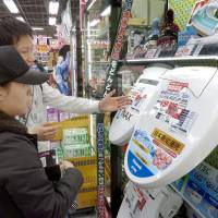 A sales clerk explains a range of washing toilet seats to a Chinese tourist at an electronics retailer in Tokyo in February. | KYODO