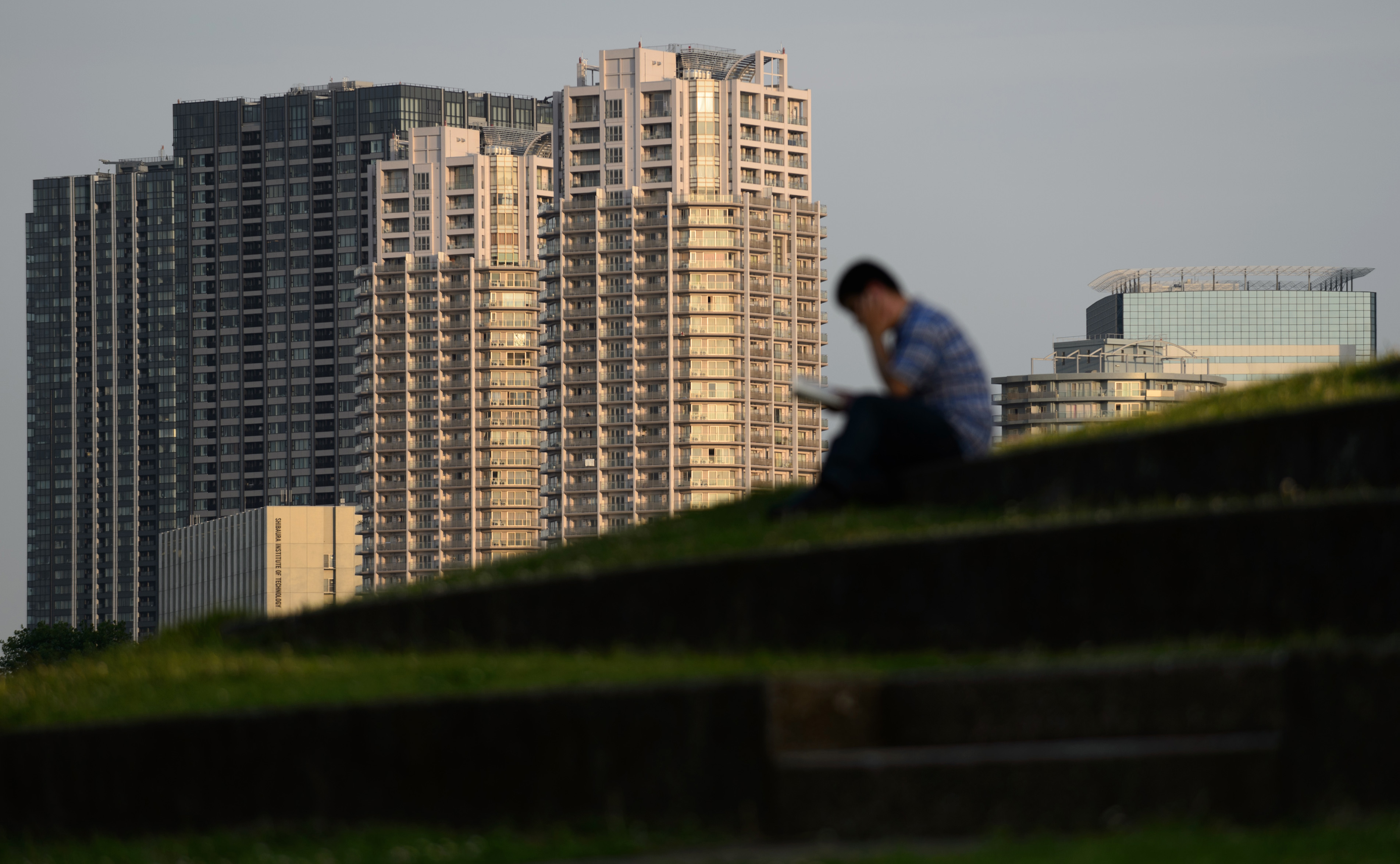 A man sits in front of residential buildings in Tokyo in June. Property prices in Tokyo are inching up as Chinese buyers flock there. | BLOOMBERG