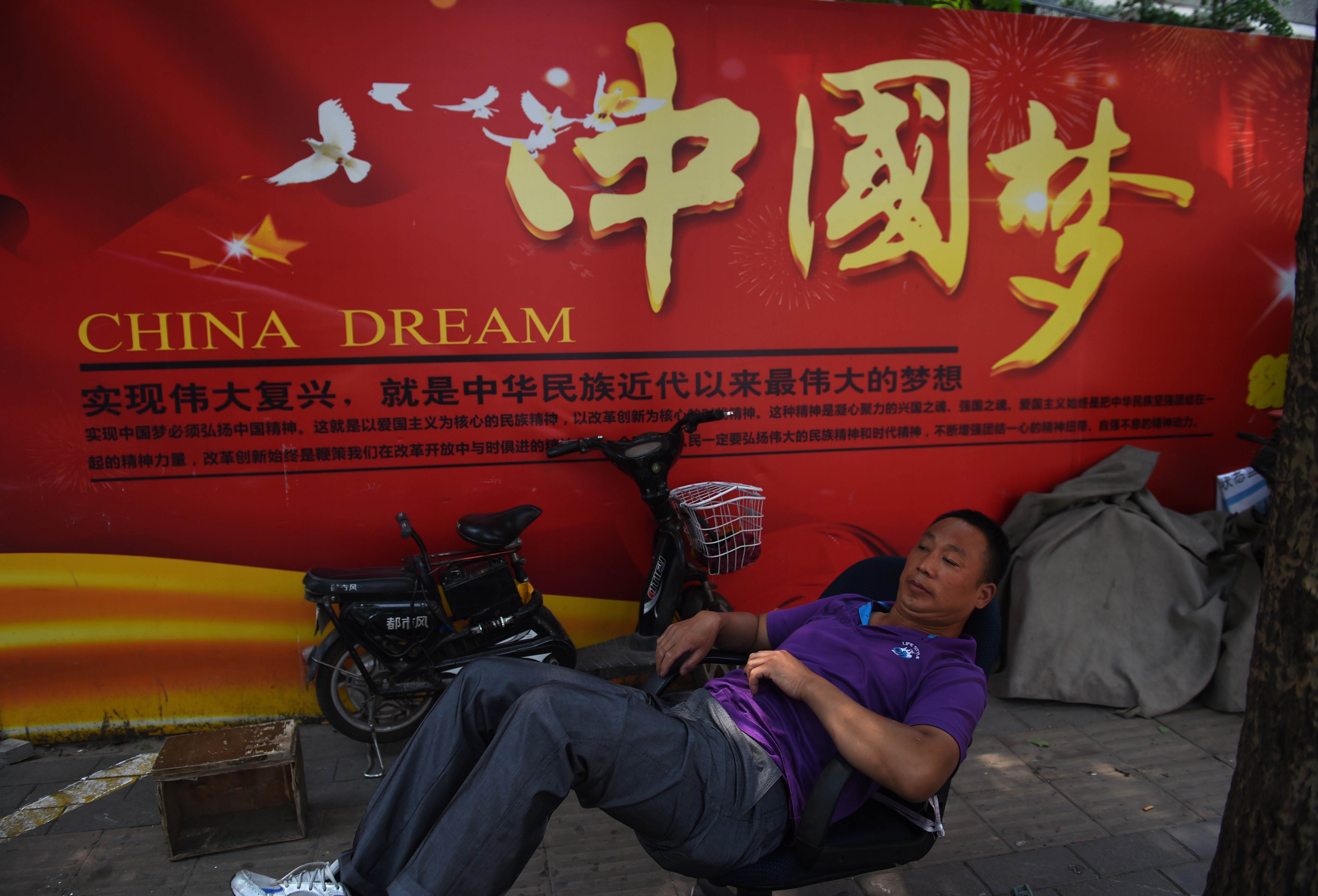 A man rests in front of a banner about the 'China Dream,' President Xi Jinping's vision for the nation's future, in Beijing on Tuesday. | AFP-JIJI