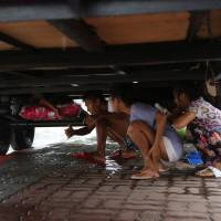 Filipinos shelter from a storm beneath a container truck as Tropical Storm Linfa enhanced the southwest monsoon in Manila on Sunday. | AP