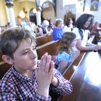 A boy and his family pray during Mass at Saint Joseph Catholic Church in Detroit on Saturday, ahead of the unveiling of a controversial goat-headed Baphomet sculpture in the city. | AP