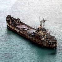 Filipino soldiers wave from the Philippine navy\'s dilapidated Sierra Madre in May. The World War II-era ship is grounded on Ayungin Shoal, also known as the Second Thomas Shoal, in the Spratly Islands. | REUTERS