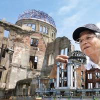 Volunteer guide Okihiro Terao stands in front of the iconic Atomic Bomb Dome with his self-made stained-glass models of the building in Hiroshima on July 15. | KYODO