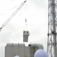 The cover shrouding the reactor 1 building at the Fukushima No. 1 nuclear plant is dismantled Tuesday as members of a Fukushima Prefectural Government safety council watch. | KYODO