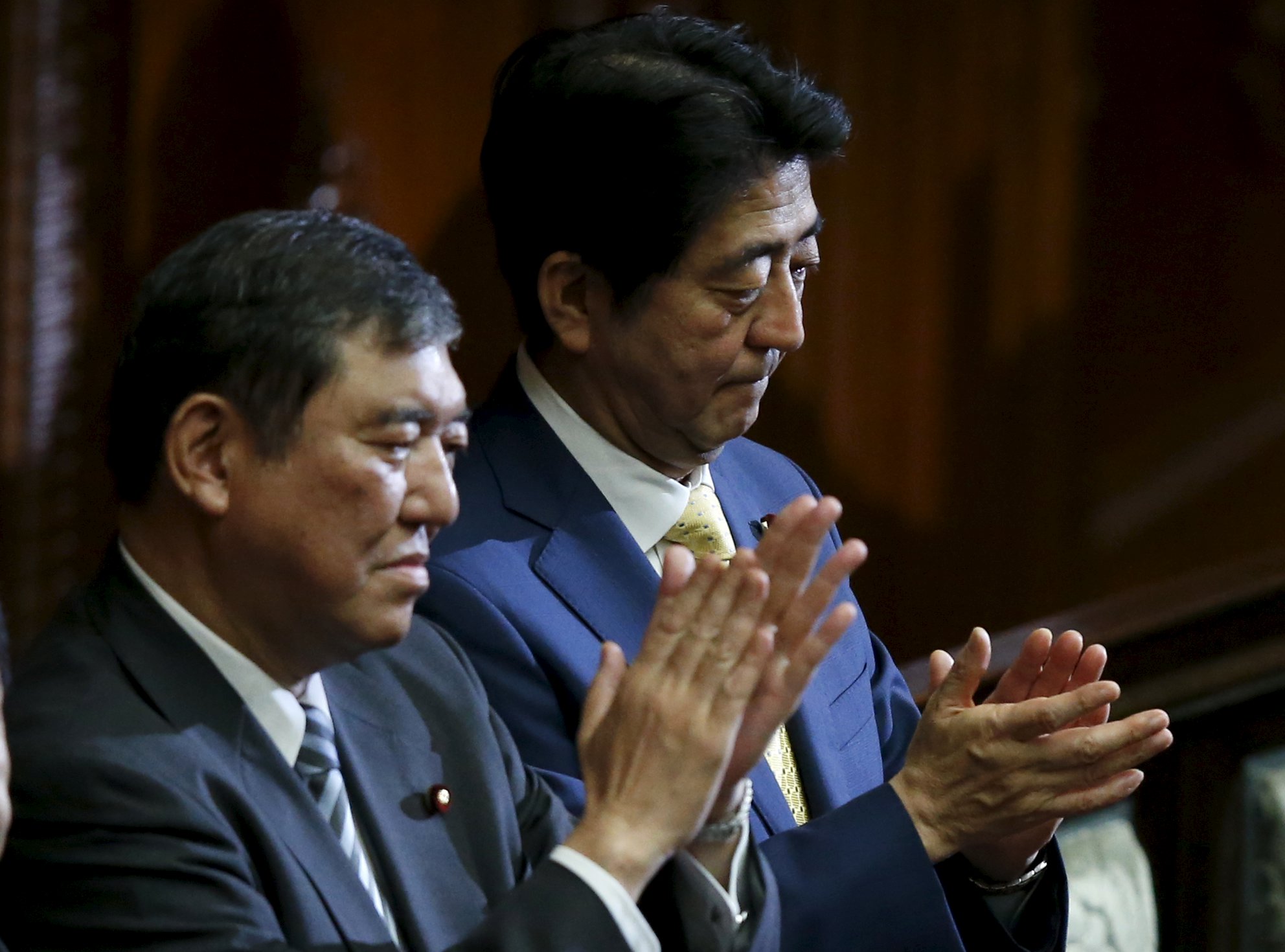 Japan's Prime Minister Shinzo Abe and minister in charge of reviving local economies Shigeru Ishiba applaud after the government-proposed security-related legislation passes in the Lower House during the plenary session of the parliament in Tokyo on Thursday. | REUTERS