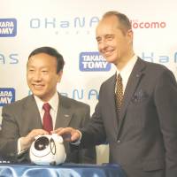 NTT Docomo President Kaoru Kato (left) and Tomy Co. President Harold Meij show off Ohanas, a communication robot that uses Docomo\'s cloud-based voice agent technology, in Tokyo on June 4. | KAZUAKI NAGATA