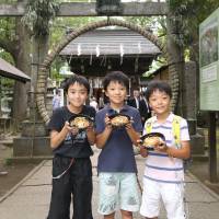 Circle of life: Three boys display their bowls of nagoshi gohan in front of a Tokyo Shinto shrine\'s ring of woven reeds. | &#169; RICE STABLE SUPPLY SUPPORT ORGANIZATION