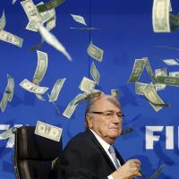 Dollar bills flutter around FIFA President Sepp Blatter after a British comedian tossed a wad of cash at him, interrupting a Monday news conference in Zurich as the scandal-tainted official was about to speak. | REUTERS