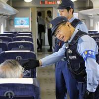 A police officer talks to a Sanyo shinkansen passenger on Friday. Police nationwide have reinforced patrols on trains and in stations after a man burned himself to death on a speeding bullet train on Tuesday and caused the death of an unrelated female passenger. | KYODO