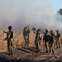 Israeli soldiers stand next to smoke from a fire caused by a rocket attack in northern Israel, near the Lebanese border, Thursday. Rockets that struck an northern Israeli village near the Lebanese border on Thursday, causing no casualties, were launched from the Syrian Golan Heights, the Israeli army said. | JIJIPIX / REUTERS