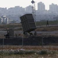 An Israeli soldier walks past an \"Iron Dome\" battery, a short-range missile defense system designed to intercept and destroy incoming short-range rockets and artillery shells, on Thursday in the city of Ashdod. | AFP-JIJI