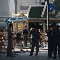 Policemen stand at the cordoned-off site of a bomb blast at the popular Erawan Shrine in the heart of Bangkok\'s tourist and commercial center on Tuesday. The death toll from a bomb blast in the Thai capital rose to 21 on Tuesday with 123 wounded, police said, adding that seven tourists, from China, Hong Kong, Malaysia and Singapore, among those killed in the attack. | AFP-JIJI