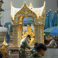 Police investigators work near the statue of Phra Phrom, which is the Thai interpretation of the Hindu god Brahma, at the Erawan Shrine the morning after an explosion in Bangkok Tuesday. | AP