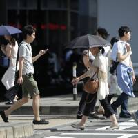 Women use parasols to shelter from the sun as they cross a street in Tokyo on July 13. | BLOOMBERG