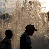 Men walk past a fountain in Nagasaki\'s Peace Park at sunset on Friday. Rising temperatures across the nation have contributed to a surge in heatstroke cases. | REUTERS