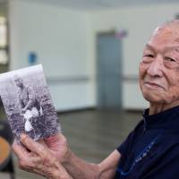 Lee Bong-moon poses with an old photograph of himself at the Hapchon Welfare Center for Atomic Bomb Survivors in Hapcheon, South Korea, in July. | BLOOMBERG