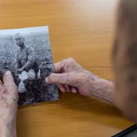 Lee Bong-moon looks at an old photograph of himself at the Hapchon Welfare Center for Atomic Bomb Survivors in Hapcheon, South Korea, in July. | BLOOMBERG