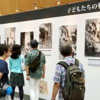 Visitors look at photographs from the end of World War II until the present day that show children at home and abroad at a photo exhibition that opened Saturday in Tokyo. | KYODO