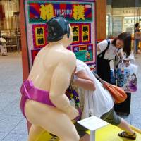 A woman tries sumo wrestling with a wrestler-shaped machine displayed at the KITTE shopping area inside JP Tower, a skyscraper in front of JR Tokyo Station, where a sumo-related exhibition is held ahead of exhibition bouts to be held there on Aug. 29. | KYODO