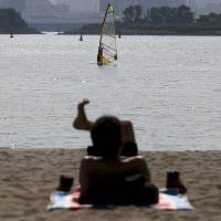 Solar power: A man soaks up some rays on the beach at Odaiba Seaside Park in Tokyo earlier this month. A recent heat wave hasn\'t led to disastrous power shortages. | REUTERS