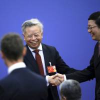 Jin Liqun (left) shakes hands with Chinese Finance Minister Lou Jiwei ahead of a signing ceremony for articles of agreement of the Asian Infrastructure Investment Bank at the Great Hall of the People in Beijing on June 29. | REUTERS