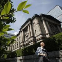 A pedestrian walks past the Bank of Japan headquarters in Tokyo. Some BOJ officials see a growing likelihood the central bank will lower its inflation outlook again. | BLOOMBERG