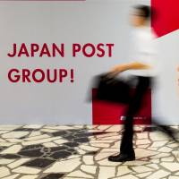 A pedestrian passes a poster at the Tokyo headquarters of Japan Post in June. Japan Post Holdings Co. and its banking and insurance units will begin trading on the Tokyo Stock Exchange on Nov. 4, the bourse announced Thursday. Japan Post valued at ¥12.61 trillion; listing set for Nov. 4