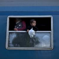 A Syrian refugee child holds a balloon fashioned from a glove while waiting with her family in a train heading for the Austrian border, in Roszke, southern Hungary, on Monday. | AP