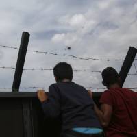 Migrants look over a fence into Hungary at the Horgos border crossing, near Horgos, Serbia, on Tuesday. | AP