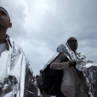 African migrant stand after arriving on a inflatable dinghy with others from Turkey on the shores of the Greek island of Lesbos on Wednesday. More than 260,000 asylum-seekers have arrived in Greece so far this year, most reaching the country\'s eastern islands on flimsy rafts or boats from the nearby Turkish coast. | AP