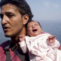 A Syrian refugee from Aleppo holds his month-old daughter moments after arriving on a dinghy on the Greek island of Lesbos on Thursday. | REUTERS