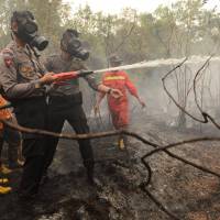 Indonesian police and firefighters extinguish a fire on burning peat land in the district of Kapuas in the Central Kalimantan province on Borneo island during President Joko Widodo\'s inspection of a firefighting operation to control agricultural and forest fires on Thursday. Under pressure from its neighbours to stop the annual haze, Indonesian President Joko Widodo has pledged to crack down on companies and individuals behind the burnings, which are a cheap but harmful way of clearing vast tracts of land for plantations. | AFP-JIJI