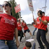 Teachers Sarah Martin (left) and Ina Shepard (with microphone) lead cheers during picketing in front of Chief Sealth International High School Wednesday in Seattle. Teachers in Seattle began walking picket lines Wednesday after last-minute negotiations over wages and other issues failed to avert a strike in Washington state\'s largest school district. | AP