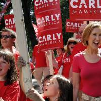 Republican presidential candidate Carly Fiorina, the former Hewlett-Packard chief executive, waves as she and supporters march in the Labor Day parade Monday in Milford, New Hampshire. She is the latest target of rival Donald Trump\'s brash comments, this time about her looks. | AP