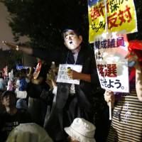 A protester in a mask depicting Prime Minister Shinzo Abe offers a mock salute during a rally against the government in front of the Diet building on Friday. Foes of security laws eager to sue government, punish ruling bloc in Upper House election