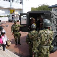 A girl waits for her mother to alight from a Self-Defense Forces vehicle, upon arrival at a gym serving as a public shelter for evacuated residents in Tsukubamirai, Ibaraki Prefecture, on Friday. | SHUSUKE MURAI