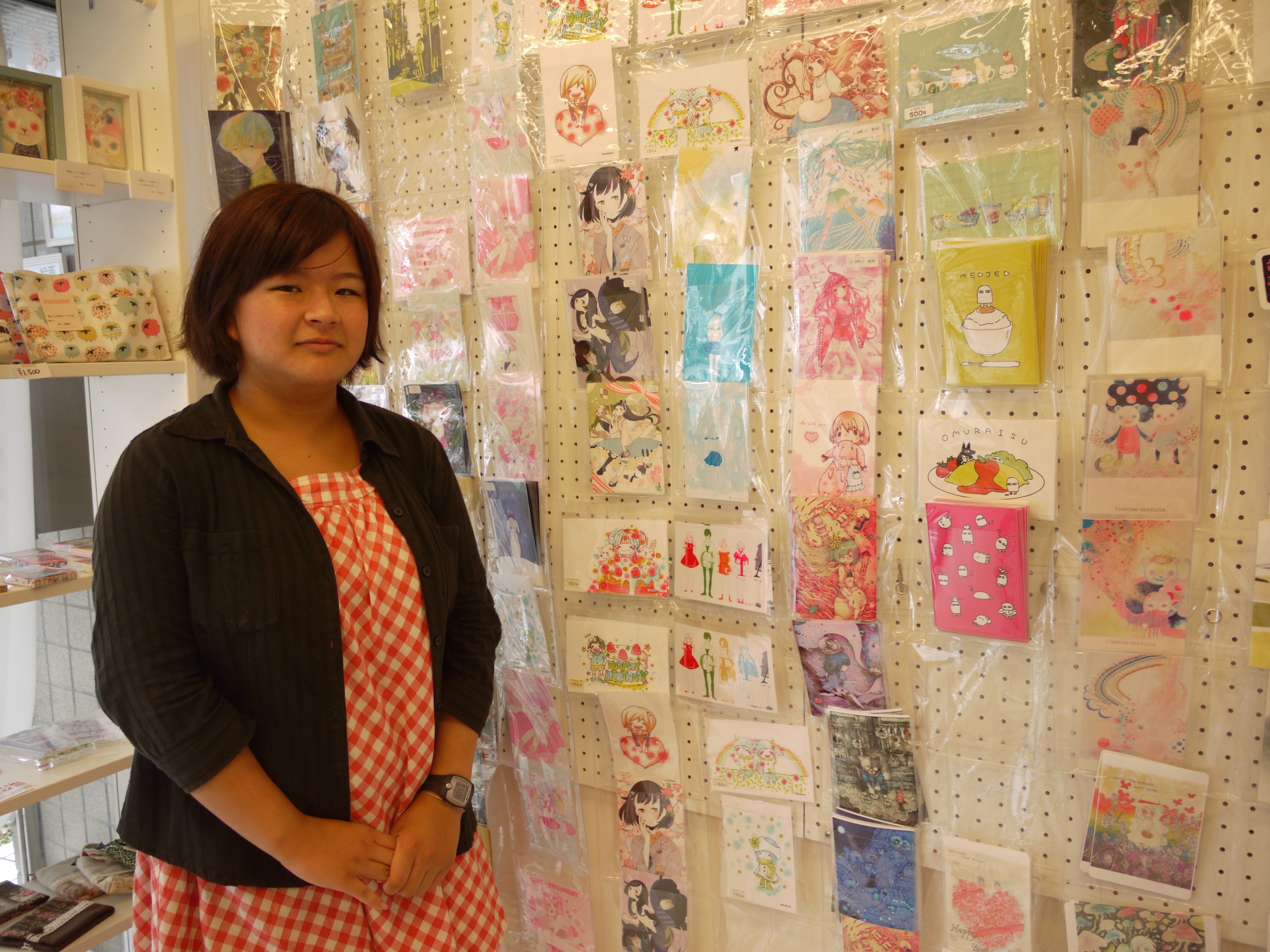 Haruka Imatoku, owner of the Nijiiro Komachi craft store in Tokyo's Kichijoji district, poses for a photo. Some of the postcards on the wall feature rainbow colors. | TOMOKO OTAKE