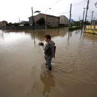 A woman holding her pet dog wades through a residential area flooded by the Kinugawa River, caused by typhoon Etau, in Joso, Ibaraki prefecture on Thursday. | REUTERS