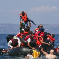 A man raises a child into the air as Syrian and Afghan refugees clamber around a deflated dinghy some 100 meters from the Greek island of Lesbos earlier this month. | REUTERS
