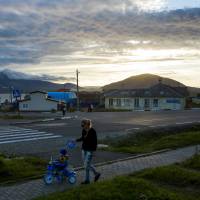 A woman pushes a child on a tricycle at sunset in the center of Yuzhno-Kurilsk, the main settlement on the southern Kuril island of Kunashiri, on Sept. 15. | REUTERS
