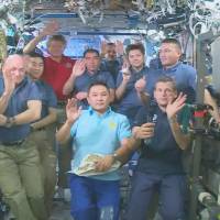 Japanese astronaut Kimiya Yui (front row second from left) and other astronauts at the International Space Station wave after a news conference late Tuesday. | NASA TV/KYODO