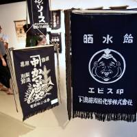 Visitors on Monday look at examples of traditional Japanese aprons called maekake at an exhibition in Itochu Aoyama Art Square in Tokyo. Worn by craftsmen and merchants in the 1960s and \'70s, maekake have recently become popular again. The exhibition runs through Sunday. | SATOKO KAWASAKI