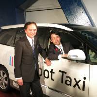 Kanagawa Gov. Yuji Kuroiwa (left) and Shinjiro Koizumi, parliamentary vice minister of the Cabinet Office, pose with an experimental self-driving car developed by Robot Taxi Inc., on Thursday in Yokohama. | KAZUAKI NAGATA