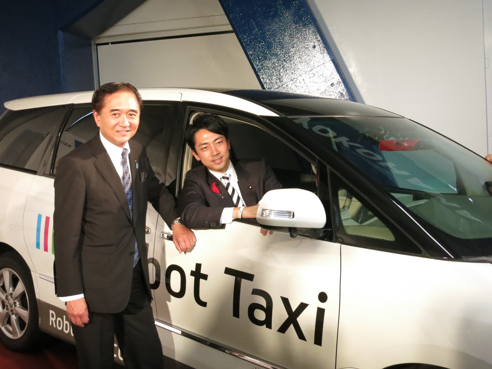 Kanagawa Gov. Yuji Kuroiwa (left) and Shinjiro Koizumi, parliamentary vice minister of the Cabinet Office, pose with an experimental self-driving car developed by Robot Taxi Inc., on Thursday in Yokohama. | KAZUAKI NAGATA
